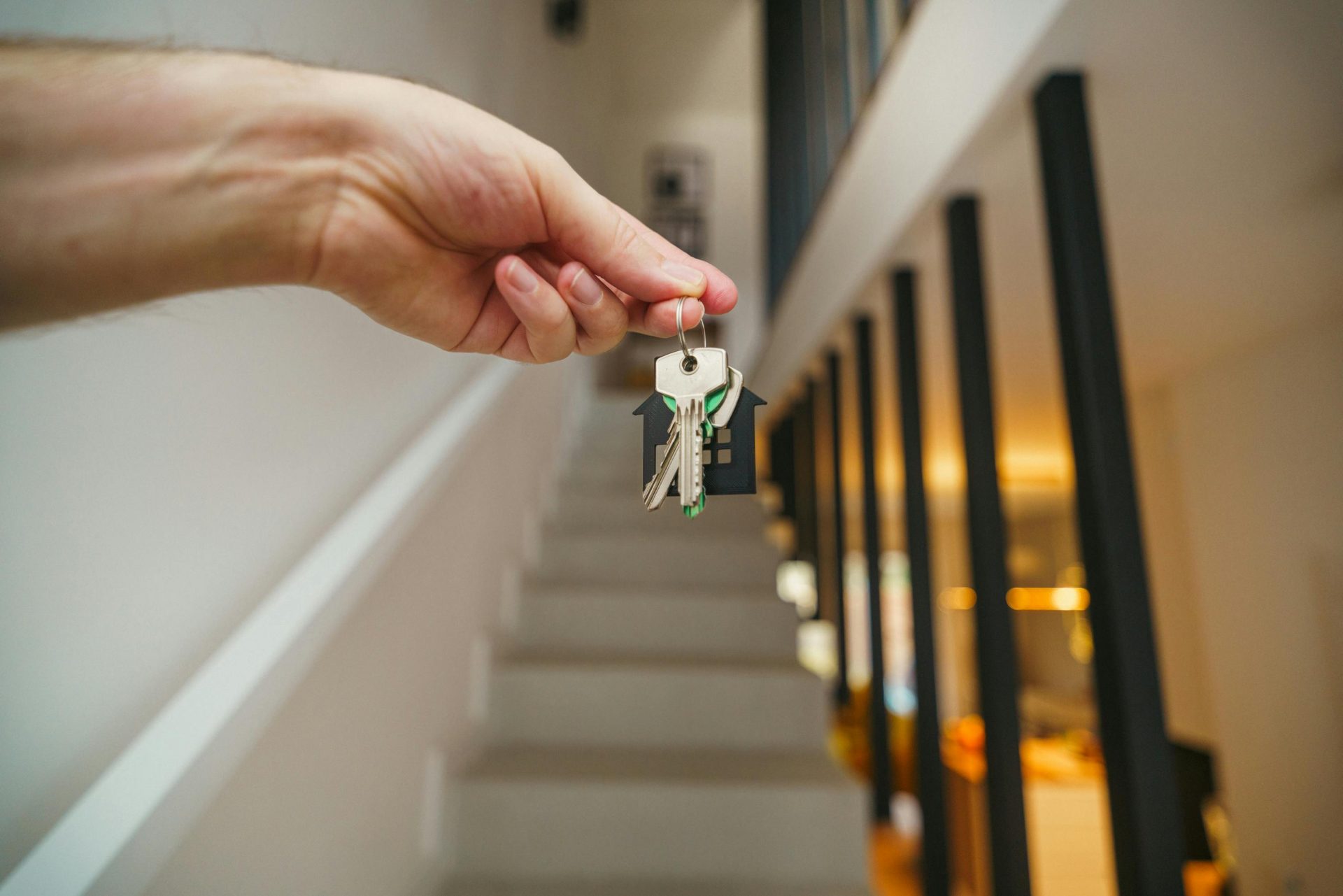A hand holding house keys in a modern interior, symbolizing new home ownership or real estate investment.